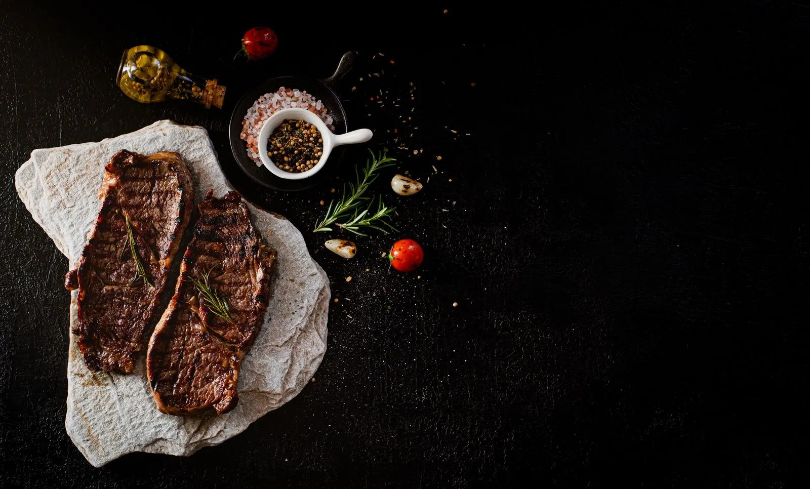 Two seasoned raw steaks on a dark table